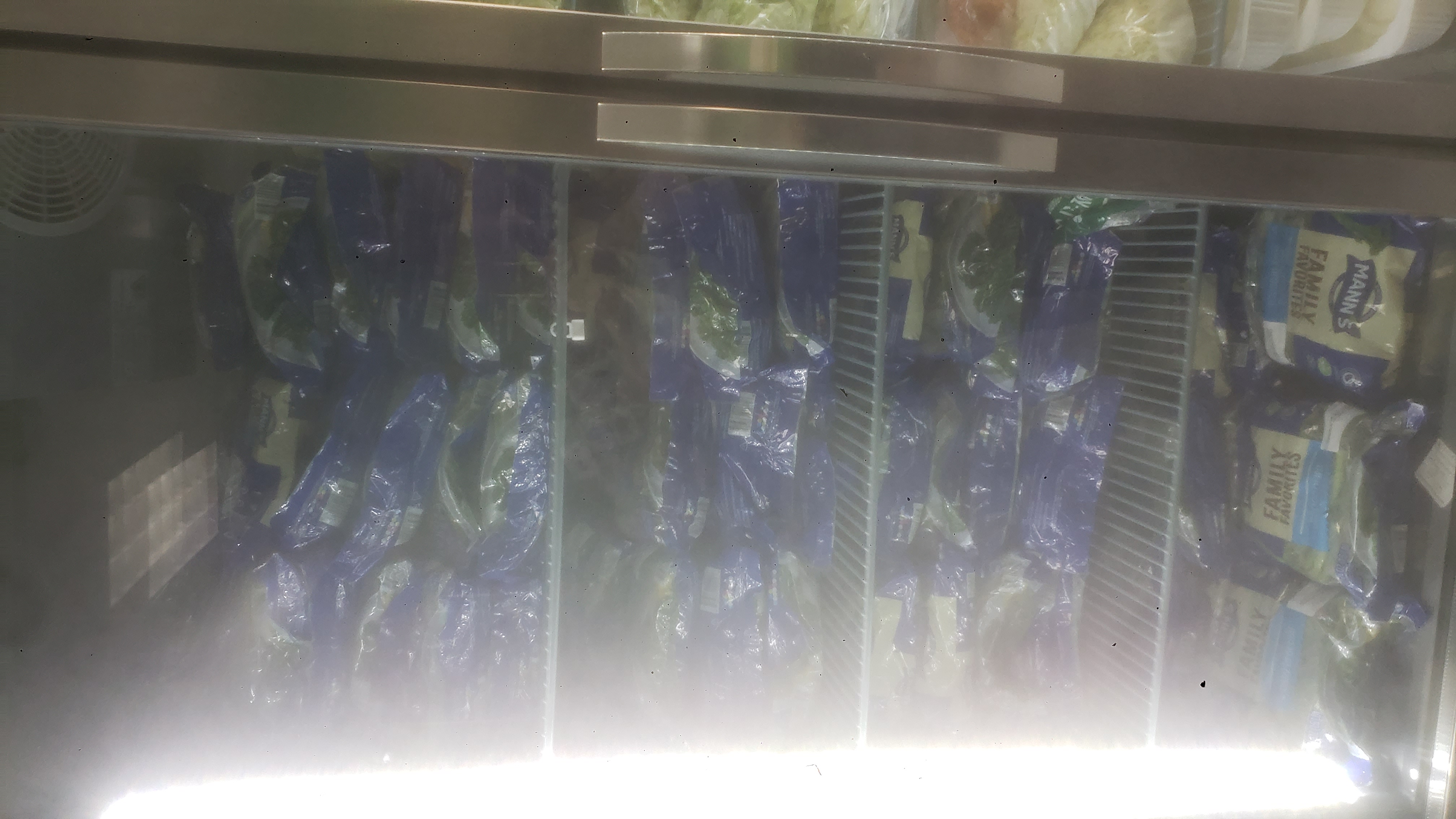 Shelves packed with bags of lettuce in a fridge.